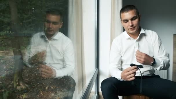 Un giovane uomo di aspetto caucasico con gli occhi marroni seduto vicino a una finestra panoramica tiene in mano una farfalla e escogita un piano aziendale. — Video Stock