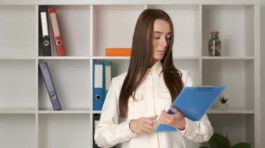 Güzel esmer, 25 yaşında, beyaz tenli, samimi bir gülümsemesi olan bir kız iş yerinde elinde bir panoyla kontratı kontrol ediyor. Şirket yöneticisi.