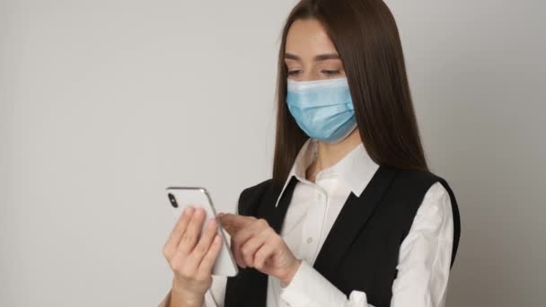 Portret kobiety pracującej w biurze w masce medycznej w celu ochrony i opieki nad zdrowym miejscem pracy podczas epidemii pandemii. Kierownik pracuje w miejscu pracy i trzyma telefon w rękach. — Wideo stockowe