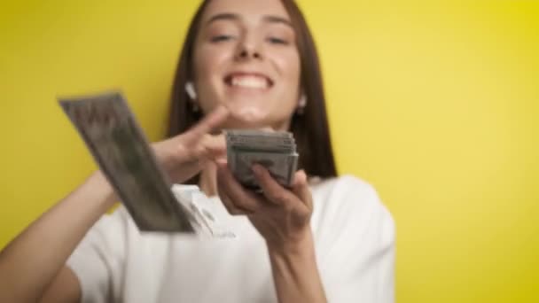 Hermosa mujer de negocios exitosa con una hermosa sonrisa dispersando billetes de 100 dólares en un fondo amarillo. Éxito y motivación — Vídeos de Stock