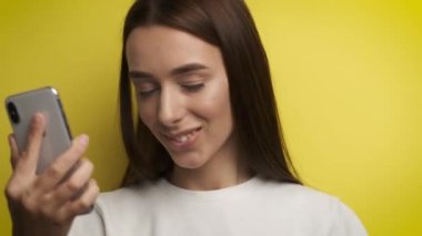 Sarı arka planda 25 yaşında güzel bir kadın kulaklıkla müzik dinliyor, dans ediyor ve telefona bakıyor.