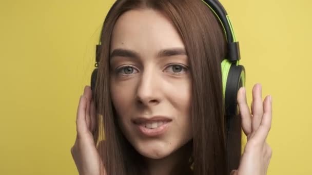 Portrait of a cute girl on a yellow background in stylish green headphones who listens to music and smiles at the camera. Active lifestyle — Stock Video