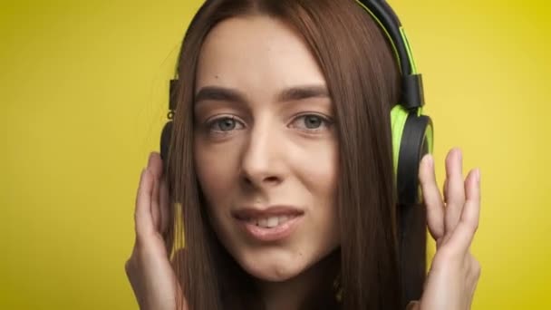 Portrait d'une jolie fille sur fond jaune dans un élégant casque vert qui écoute de la musique et sourit à la caméra. Mode de vie actif — Video