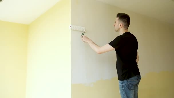 Young brunette master makes repairs in a large spacious office with panoramic windows. Painting the walls with a brush in white — Stock Video