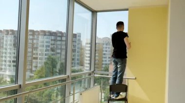 Genç işadamı geniş ofisinde panoramik pencerelerle tamirat yapıyor. Duvarları beyaza boyuyorum.