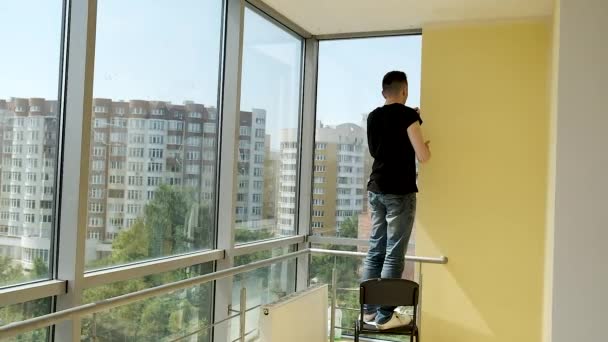 Jovem empresário faz reparos em seu escritório espaçoso com janelas panorâmicas. Pintura das paredes em branco — Vídeo de Stock