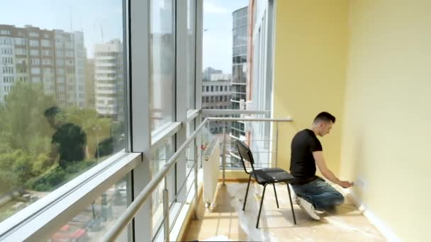Jeune homme d'affaires fait des réparations dans son bureau spacieux avec des fenêtres panoramiques. Peindre avec un pinceau les murs en blanc — Video