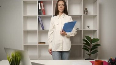 Genç, güzel bir avukat elinde bir klasörle masaüstüne yaklaşıyor ve kameraya gülümsüyor.