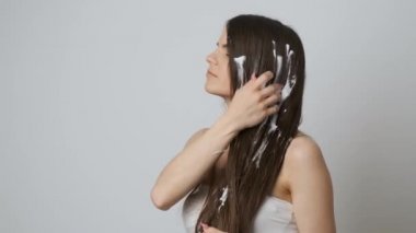 Esmer, banyodaki saçlara krema sürüyor. Kız kendine spa tedavisi uyguluyor.