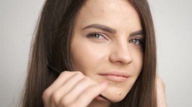 Siyah gözlü güzel bir kadın aynanın önünde duruyor ve uzun saçlarını tarıyor.