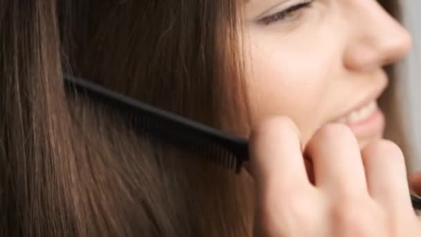 Красива жінка з чорними очима стоїть перед дзеркалом у ванній кімнаті і розчісує її довге волосся — стокове відео