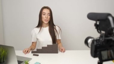 Gülümseyen genç bayan blogcu evde oturmuş konuşuyor, kameraya bakıyor ve video konferansı yapıyor. Evden çalış.