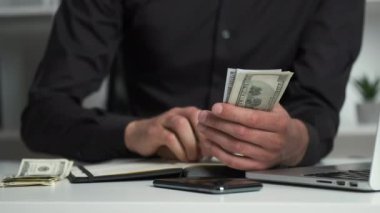 Keskin gözlü bir ofis çalışanı parayı sayar ve bir deftere yazar. Muhasebeci maaş veriyor.