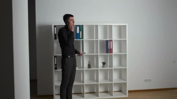 Young brunette in a black shirt walks around the office in the evening and talks on the phone solving work moments holding money in his hands — Stock Video