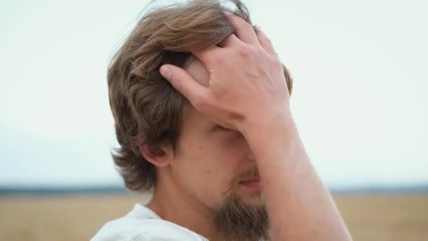 Een jonge baard brunette boer staat in een veld en bewondert de oogst en de natuur rechttrekken zijn haar en het zetten van een strohoed — Stockvideo