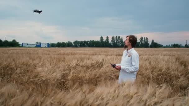 25-jarige jonge boer van blanke verschijning in geel controleert een tarwe geel veld met een drone — Stockvideo