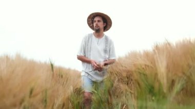Kafkas görünümlü, şapkalı ve sakallı şık bir çiftçi tarlada yürüyor ve buğday hasadına bakıyor.