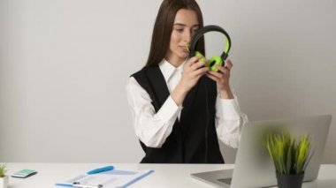 Ofiste oturan mutlu kadın dizüstü bilgisayarda çalışıyor ve kulaklıkla müzik dinliyor.