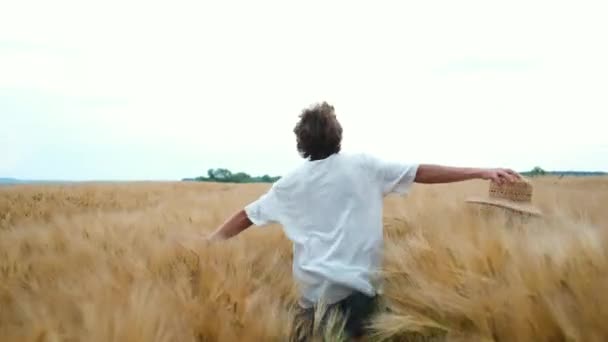 Mladý úspěšný farmář v lehkých šatech a klobouku šťastně běží přes pole a užívá si své práce — Stock video