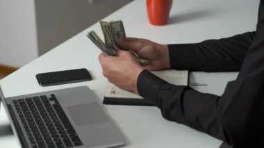 Keskin gözlü bir ofis çalışanı parayı sayar ve bir deftere yazar. Muhasebeci maaş veriyor.