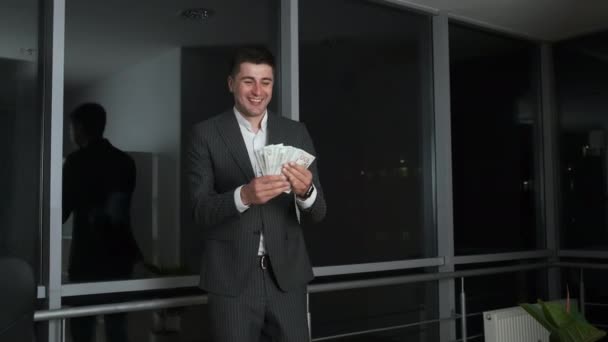 Snygg framgångsrik 30-årig brunett i kostym dans på kontoret med utsikt över nattstaden och sprida pengar glatt — Stockvideo