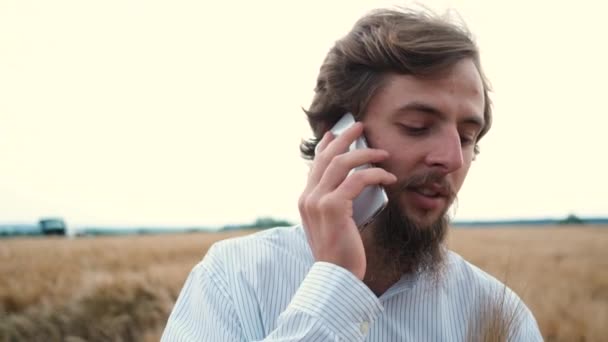 Młody biały rolnik chodzi po polu, sprawdza plony i rozmawia przez telefon. — Wideo stockowe