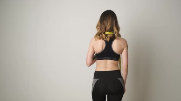 Portret van een slank meisje van blanke afkomst in sportkleding staand met een meetlint en drinkwater na de training — Stockvideo