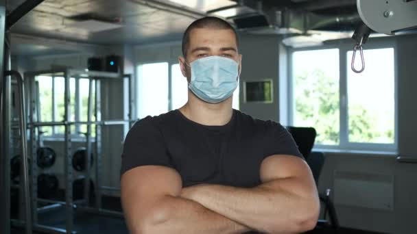 Спортсмен з великими біцепсами стоїть в спортзалі в масці чоловіка з складеними руками — стокове відео