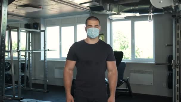 Porträtt av en atletisk kille med stora biceps som passar i gymmet till kameran och sätter händerna upp — Stockvideo
