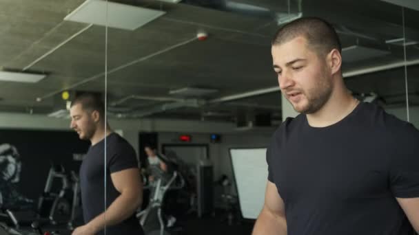 Portrét atletického chlapa s velkými biceps zahřívání na běžícím pásu před cvičením v tělocvičně — Stock video