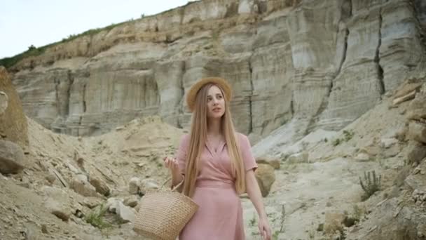 Touriste jeune femme d'apparence caucasienne blonde dans une robe rose avec une capuche et un sac à main marche à travers le canyon et profite de la beauté du sable — Video