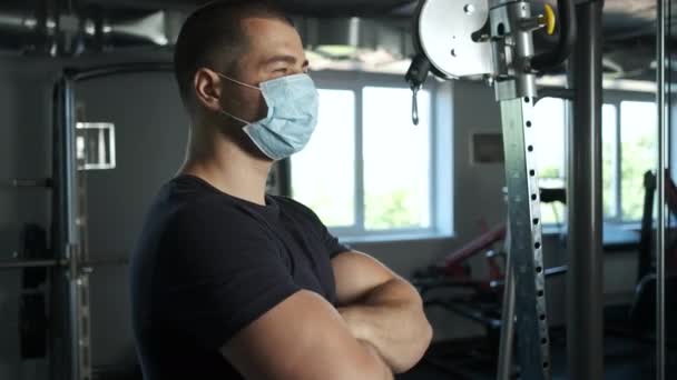 Atletisk man med stora biceps står i gymmet i en mask i en hane med händerna vikta — Stockvideo
