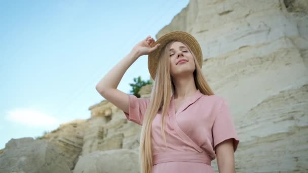 身穿粉色连衣裙、头戴头巾、头戴手提包、长相白皙、金发碧眼的游客年轻女子穿过峡谷，尽享沙滩之美 — 图库视频影像