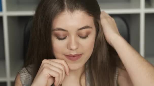 Retrato de una mujer hermosa en un traje con una sonrisa sincera, senos exuberantes y cabello largo sentado en la oficina — Vídeos de Stock