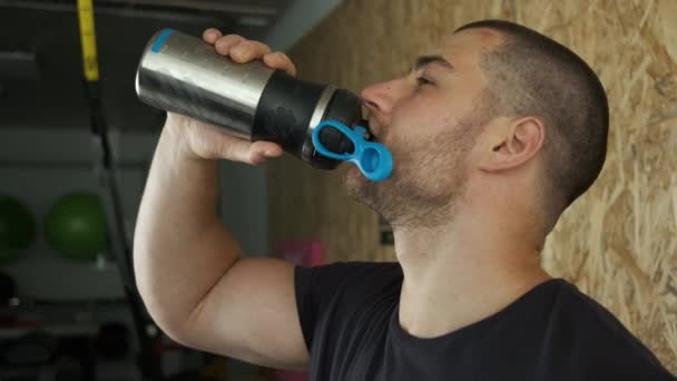 Un joven atleta en el gimnasio bebe agua y botellas después del entrenamiento — Vídeos de Stock