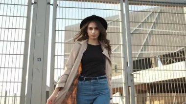 Genç ve güzel bir kız sokakta yürüyor. Siyah şapkalı, kahverengi pelerinli, uzun saçlı bir esmer. Arkadan portre çerçevesi