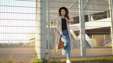 Genç ve güzel bir kız sokakta yürüyor. Siyah şapkalı, kahverengi pelerinli, uzun saçlı bir esmer. Arkadan portre çerçevesi