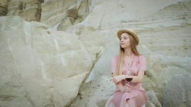 25 yaşında, sarı şapkalı, beyaz tenli bir turist bir taş ocağında bir taşın üzerinde oturur ve bir bardak kırmızı şarap içer ve dinlenir. Kanyonun tadını çıkarıyorum..