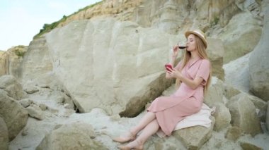 25 yaşındaki sarışın turist, beyaz şapkalı. Kum madeninde bir taşın üzerinde oturuyor ve bir bardak kırmızı şarap içiyor. Kanyonun tadını çıkarıyor.