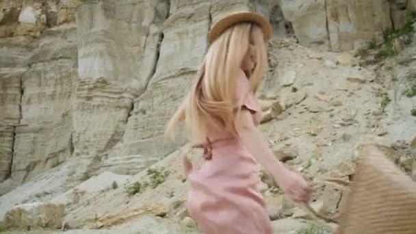 Touriste jeune femme d'apparence caucasienne blonde dans une robe rose avec une capuche et un sac à main marche à travers le canyon et profite de la beauté du sable — Video