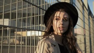 Güzel kız model sokakta dikilip kameranın önünde poz veriyor. Siyah şapkalı, kahverengi pelerinli, uzun saçlı esmer kadın. Portre çerçevesi