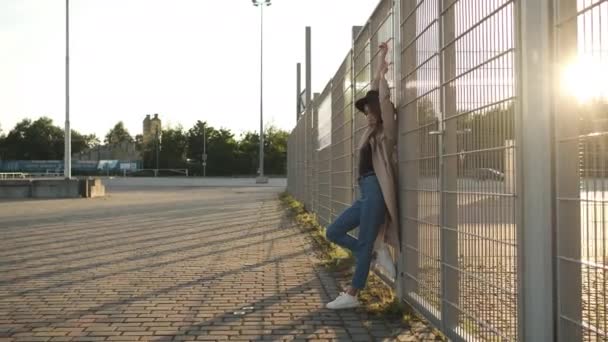 Hermosa chica modelo de pie y se pone un sombrero en la calle. Morena con el pelo largo en un sombrero negro y capa marrón. Marco de retrato desde la parte posterior — Vídeo de stock