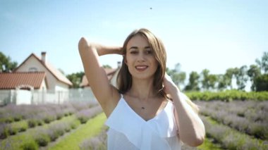 Beyaz elbiseli, uzun saçlı ve lavanta tarlasında yürüyen samimi bir gülümsemesi olan esmer bir kızın portresi. Lavanta