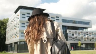 Güzel bir kız caddede güzel bir iş merkezinin yakınında yürüyor. Siyah şapkalı, kahverengi pelerinli, uzun saçlı esmer kadın. Arkadan portre çerçevesi