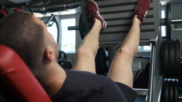 Um jovem atleta bombeado faz outro exercício de perna no ginásio em preparação para a competição. Estilo de vida saudável — Vídeo de Stock