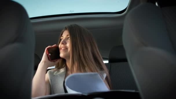 Успешная белая женщина в стильном костюме сидит в машине и решает рабочие вопросы, разговаривая по телефону — стоковое видео