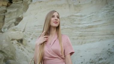 Kafkas görünümlü, pembe elbiseli, kapüşonlu ve çantalı genç bir kadın kanyonda yürüyor ve kumların güzelliğinin tadını çıkarıyor.