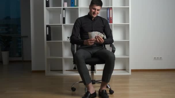 Handsome smiling businessman in a black shirt counts and happily scatters money around the office after a successful project — Stock Video