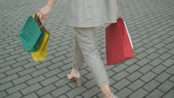 Mujer con un elegante traje gris y escote abierto regresa de una tienda, bolsas de regalo. Edificios modernos — Vídeos de Stock