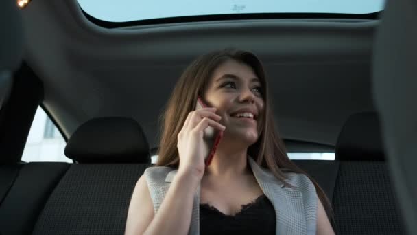 Gyönyörű üzletasszony szürke öltönyben ül egy autóban, panorámás tetővel, és beszél a telefon megoldása munka pillanatok — Stock videók
